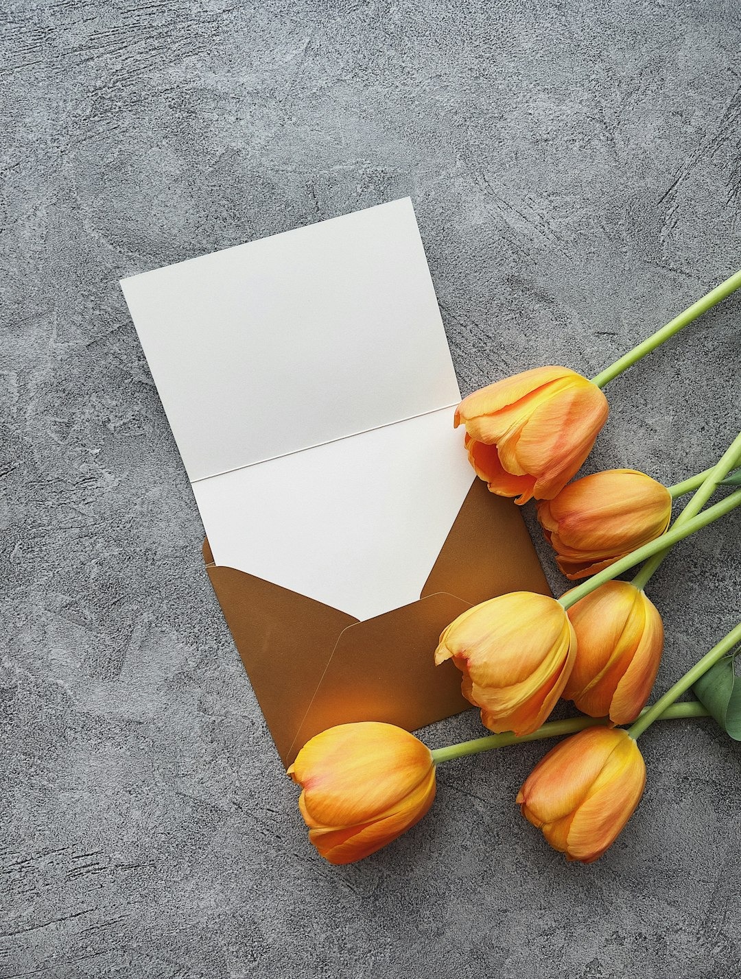 Open greeting card and orange tulips on a textured surface.